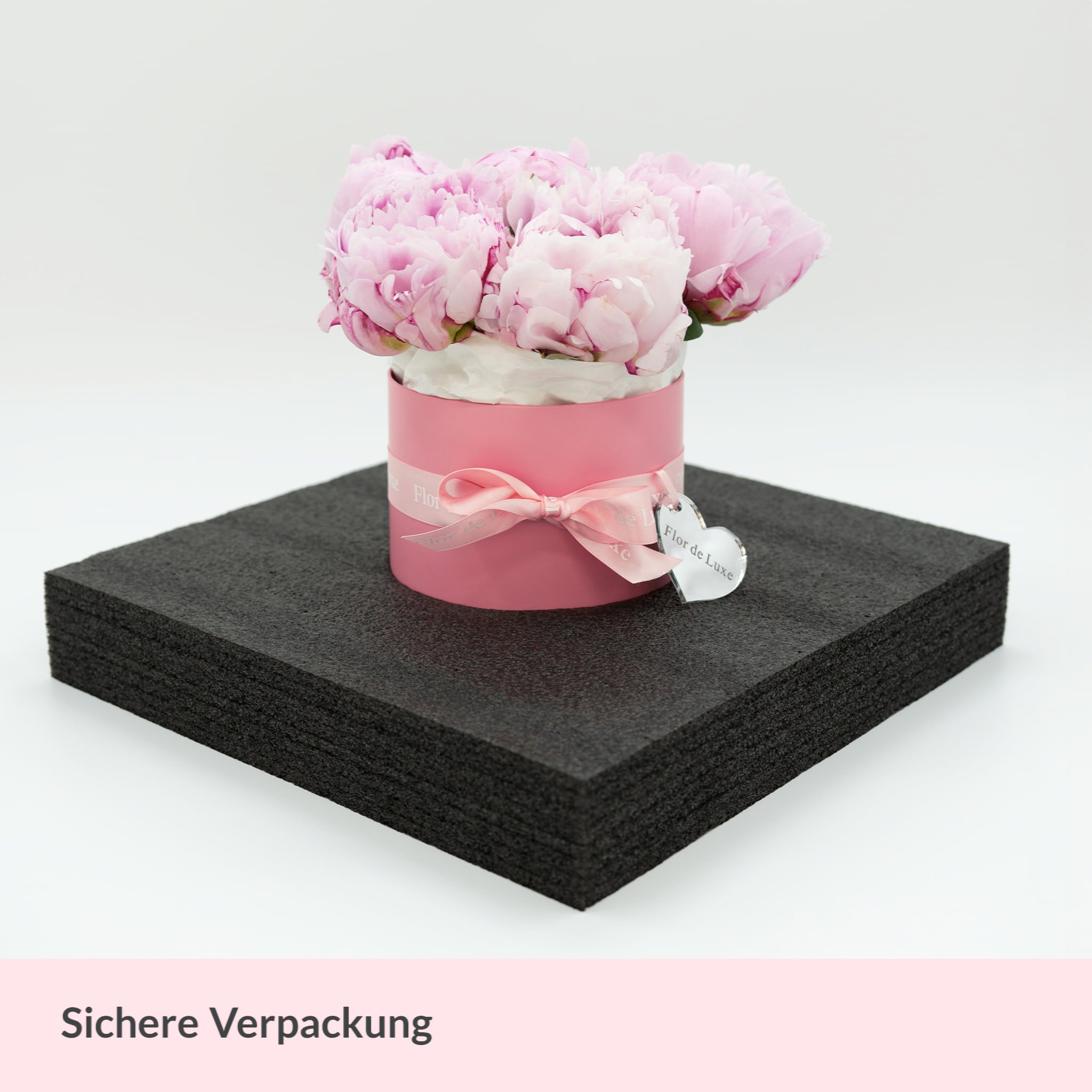 Flor de Luxe Blumenbox, sorgfältig verpackt in Sicherungsschaum für sicheren Versand, inklusive Schleife und Herzanhänger..